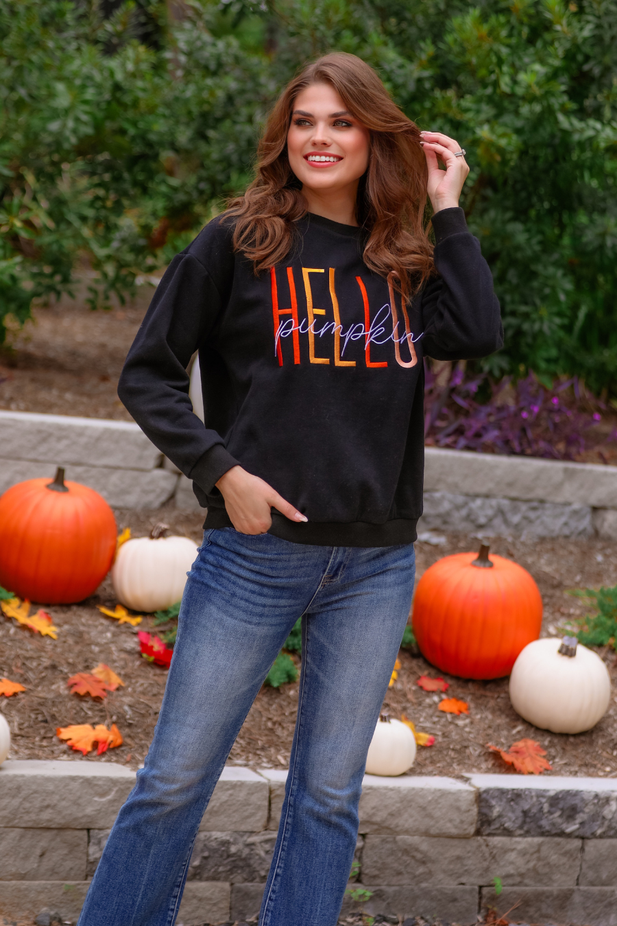 black long-sleeve sweatshirt made of soft mid-weight fabric with a crew neckline, straight hem, and colorful embroidered mix of 'HELLO' in uppercase letters (orange, rose gold, and yellow) and 'PUMPKIN' in white script handwriting