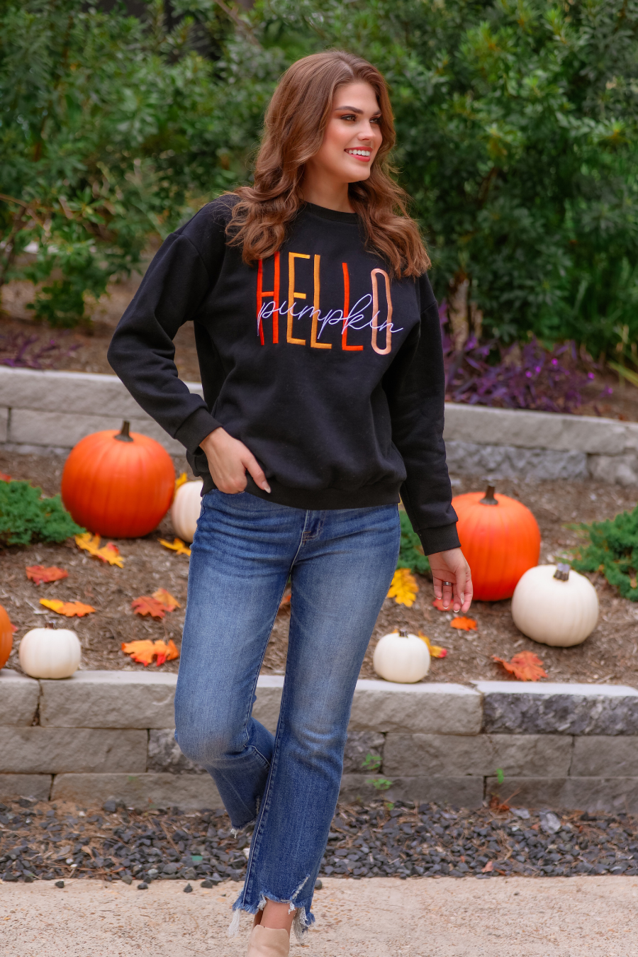 black long-sleeve sweatshirt made of soft mid-weight fabric with a crew neckline, straight hem, and colorful embroidered mix of 'HELLO' in uppercase letters (orange, rose gold, and yellow) and 'PUMPKIN' in white script handwriting