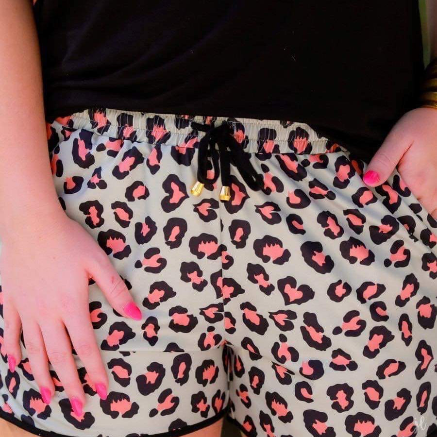 mid-rise relaxed fit activewear shorts with side pockets and a tie waist drawstring with gold bead accents, designed on a black and orange leopard pattern print fabric, olive base, and black trim