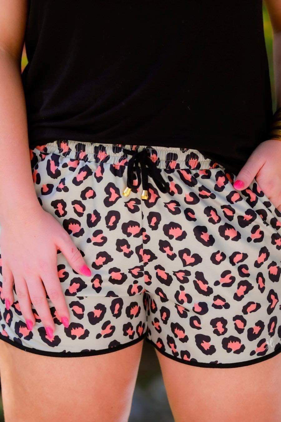 mid-rise relaxed fit activewear shorts with side pockets and a tie waist drawstring with gold bead accents, designed on a black and orange leopard pattern print fabric, olive base, and black trim