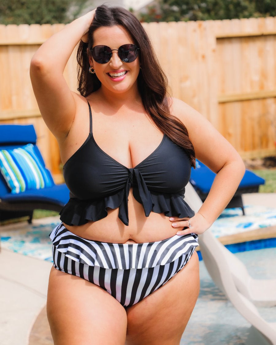 a solid black bikini top with a front tie, ruffle trim, and adjustable spaghetti straps paired with a vertical black and white full-coverage bottom with ruffle trim