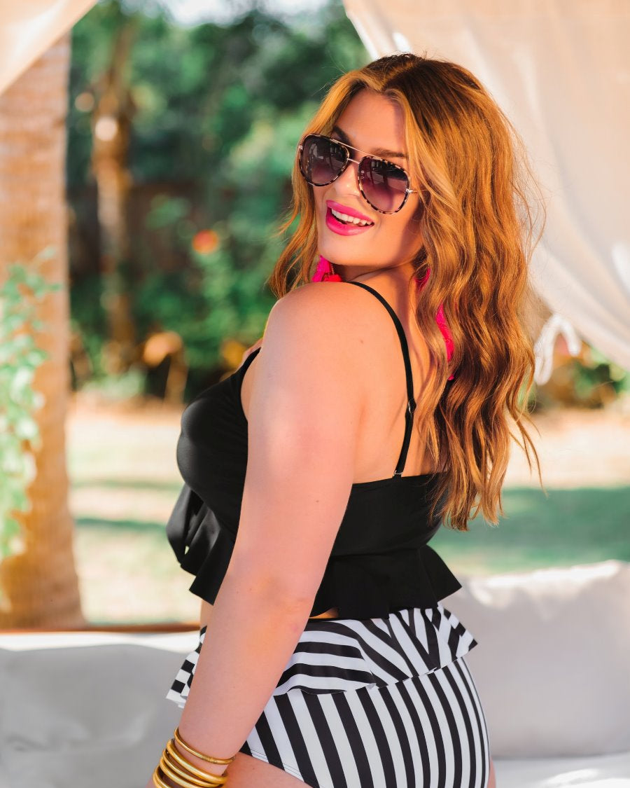 a solid black bikini top with a front tie, ruffle trim, and adjustable spaghetti straps paired with a vertical black and white full-coverage bottom with ruffle trim