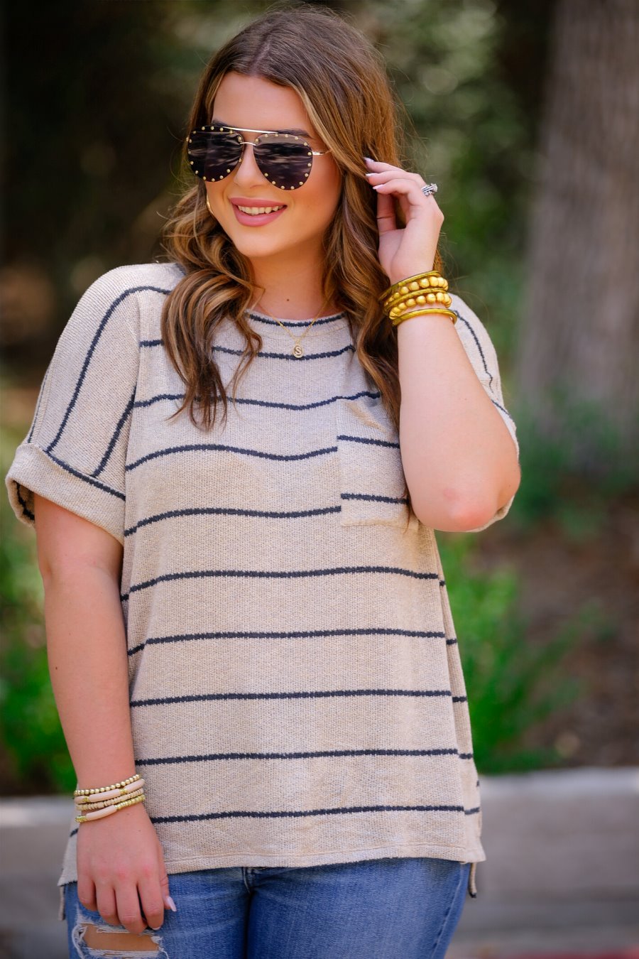 short-sleeve top made of a soft knit fabric with horizontal stripes, a rounded neckline, rolled cuffs, a front check pocket, and a relaxed silhouette on a taupe base
