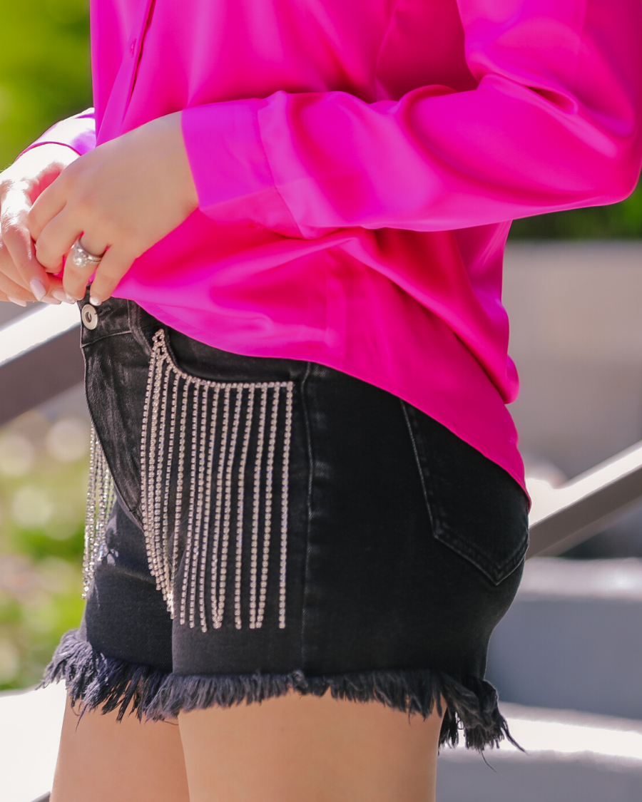 mid-rise black denim shorts with rhinestone fringe, a frayed hem, zip button-up fly with belt loops, and classic five-pocket style
