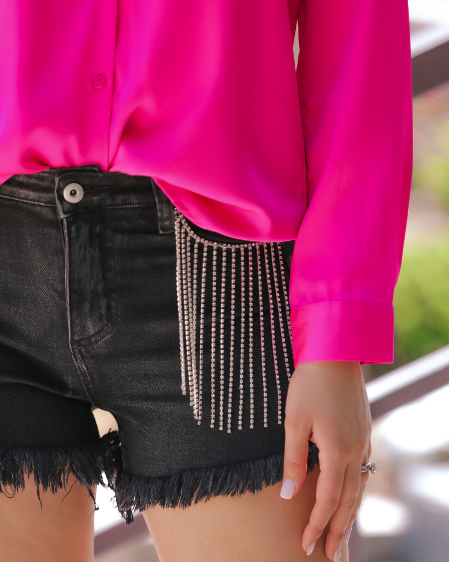 mid-rise black denim shorts with rhinestone fringe, a frayed hem, zip button-up fly with belt loops, and classic five-pocket style