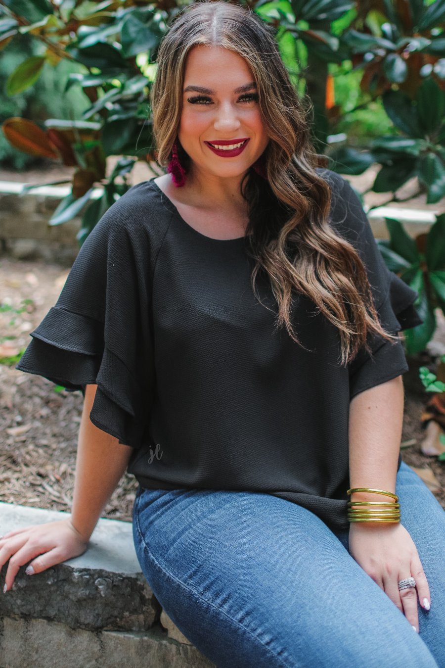 a black true-to-size blouse crafted from lightweight textured fabric with a rounded neckline, tiered ruffle sleeves, and a relaxed drape