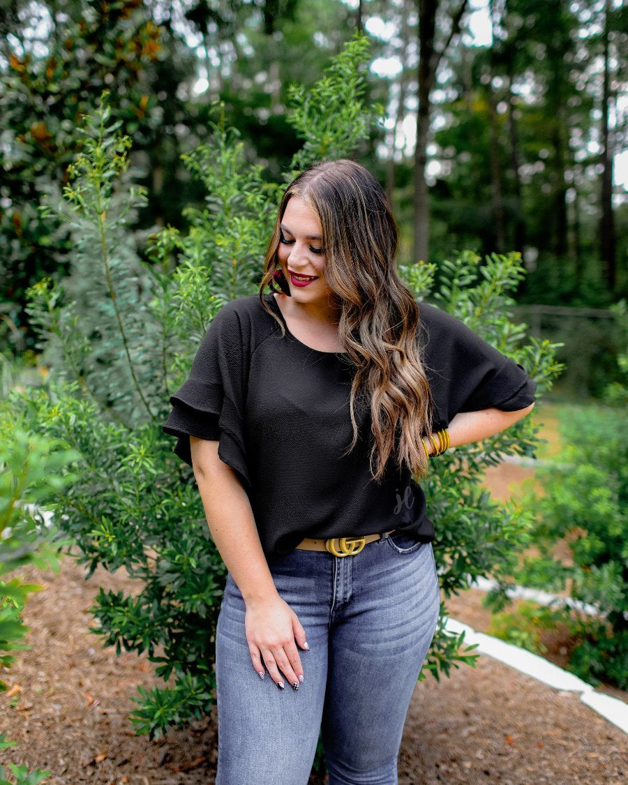 a black true-to-size blouse crafted from lightweight textured fabric with a rounded neckline, tiered ruffle sleeves, and a relaxed drape