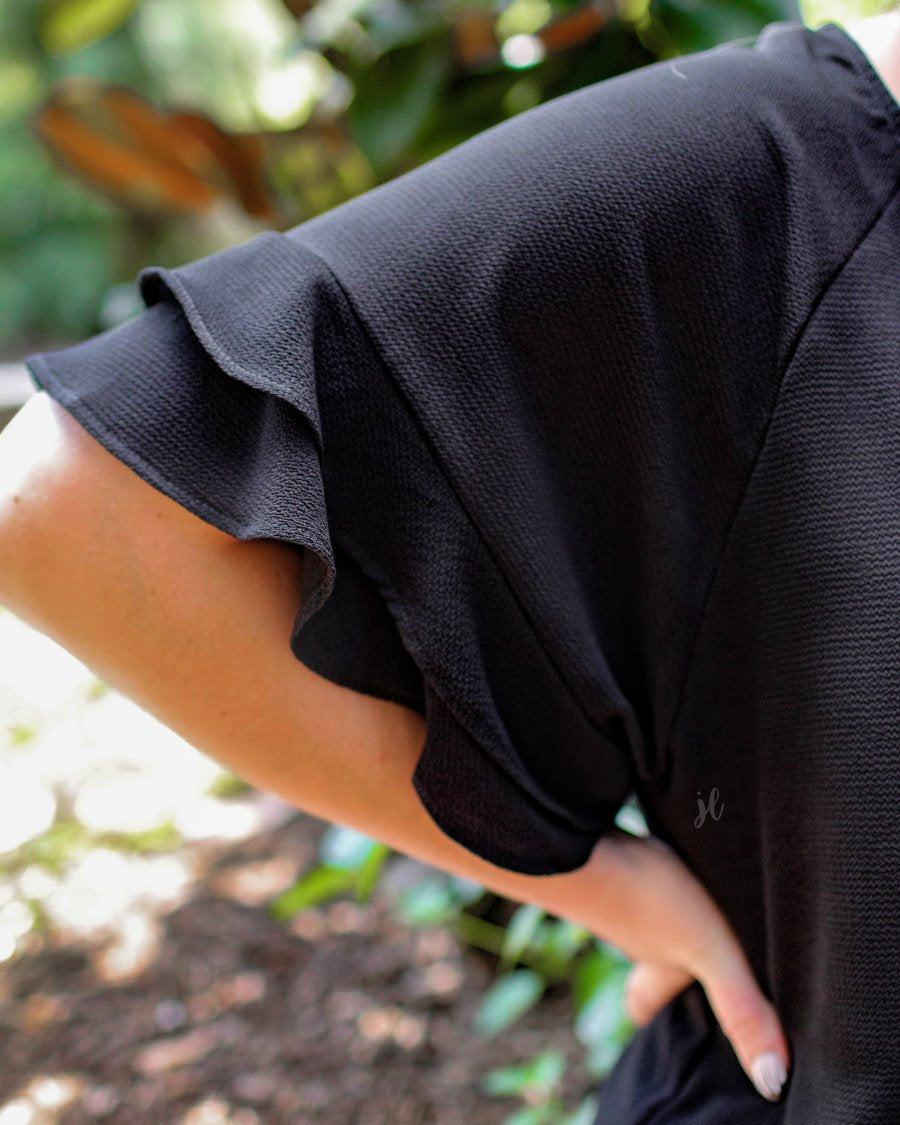 a black true-to-size blouse crafted from lightweight textured fabric with a rounded neckline, tiered ruffle sleeves, and a relaxed drape
