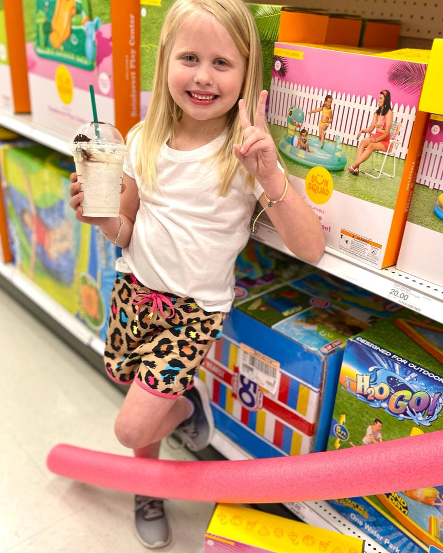 mid-rise relaxed fit activewear shorts with side pockets and a tie waist drawstring with gold bead accents, designed on a vibrant multicolor leopard pattern print fabric, tan base, and pink trim