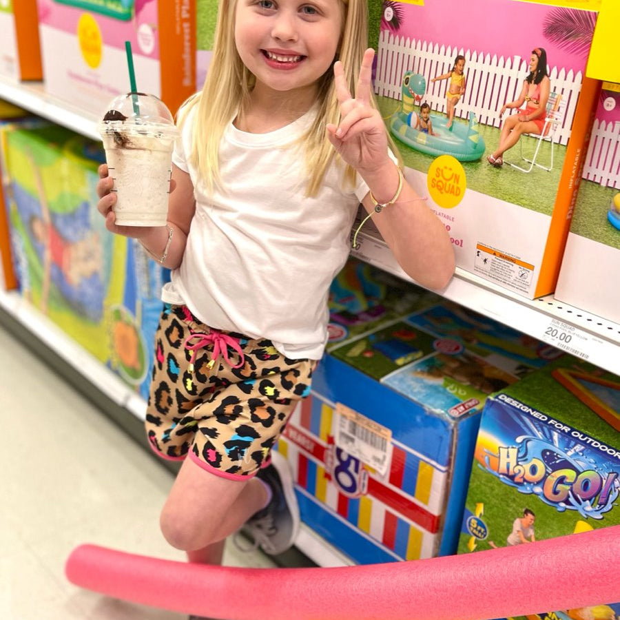 mid-rise relaxed fit activewear shorts with side pockets and a tie waist drawstring with gold bead accents, designed on a vibrant multicolor leopard pattern print fabric, tan base, and pink trim
