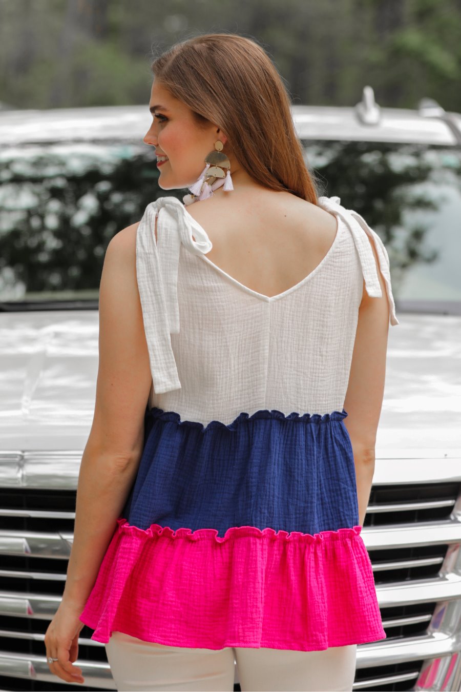 a pink tiered color block top with a V-neckline front and back, adjustable wide tie straps, a ruffled hem, and a relaxed, lightweight fit