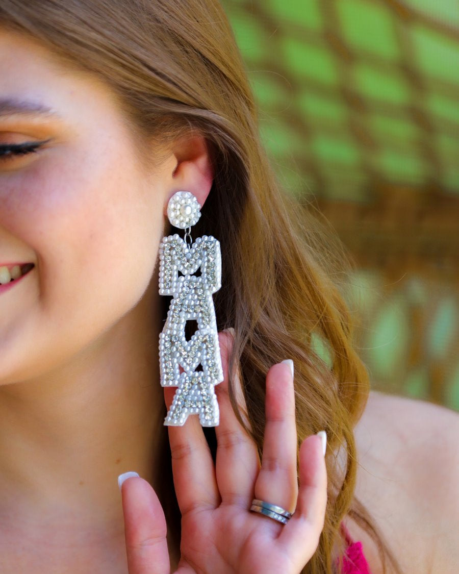 oversized dangle drop earrings with stacked 'MAMA' lettering in luminous white pearls and shimmering silver rhinestones, a pearl accented stud top, a comfort back earring with a plastic disc stopper in gold, and a white felt back