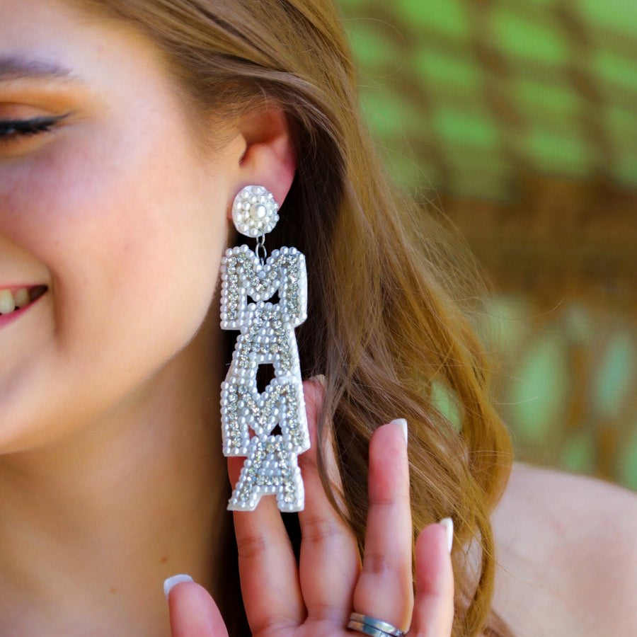 oversized dangle drop earrings with stacked 'MAMA' lettering in luminous white pearls and shimmering silver rhinestones, a pearl accented stud top, a comfort back earring with a plastic disc stopper in gold, and a white felt back