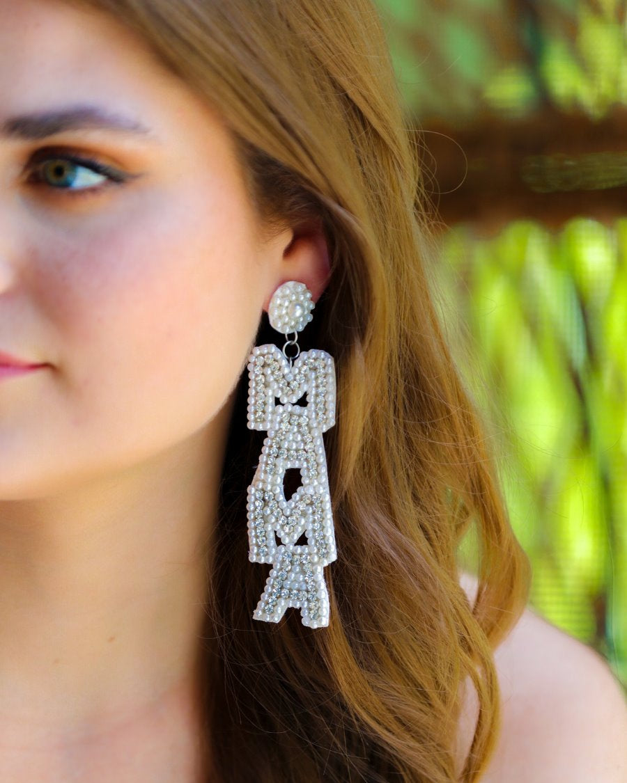 oversized dangle drop earrings with stacked 'MAMA' lettering in luminous white pearls and shimmering silver rhinestones, a pearl accented stud top, a comfort back earring with a plastic disc stopper in gold, and a white felt back