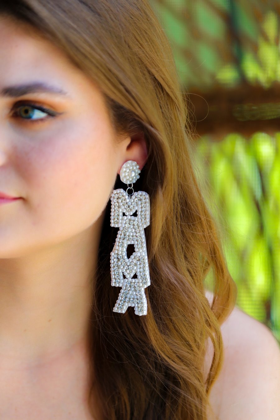 oversized dangle drop earrings with stacked 'MAMA' lettering in luminous white pearls and shimmering silver rhinestones, a pearl accented stud top, a comfort back earring with a plastic disc stopper in gold, and a white felt back