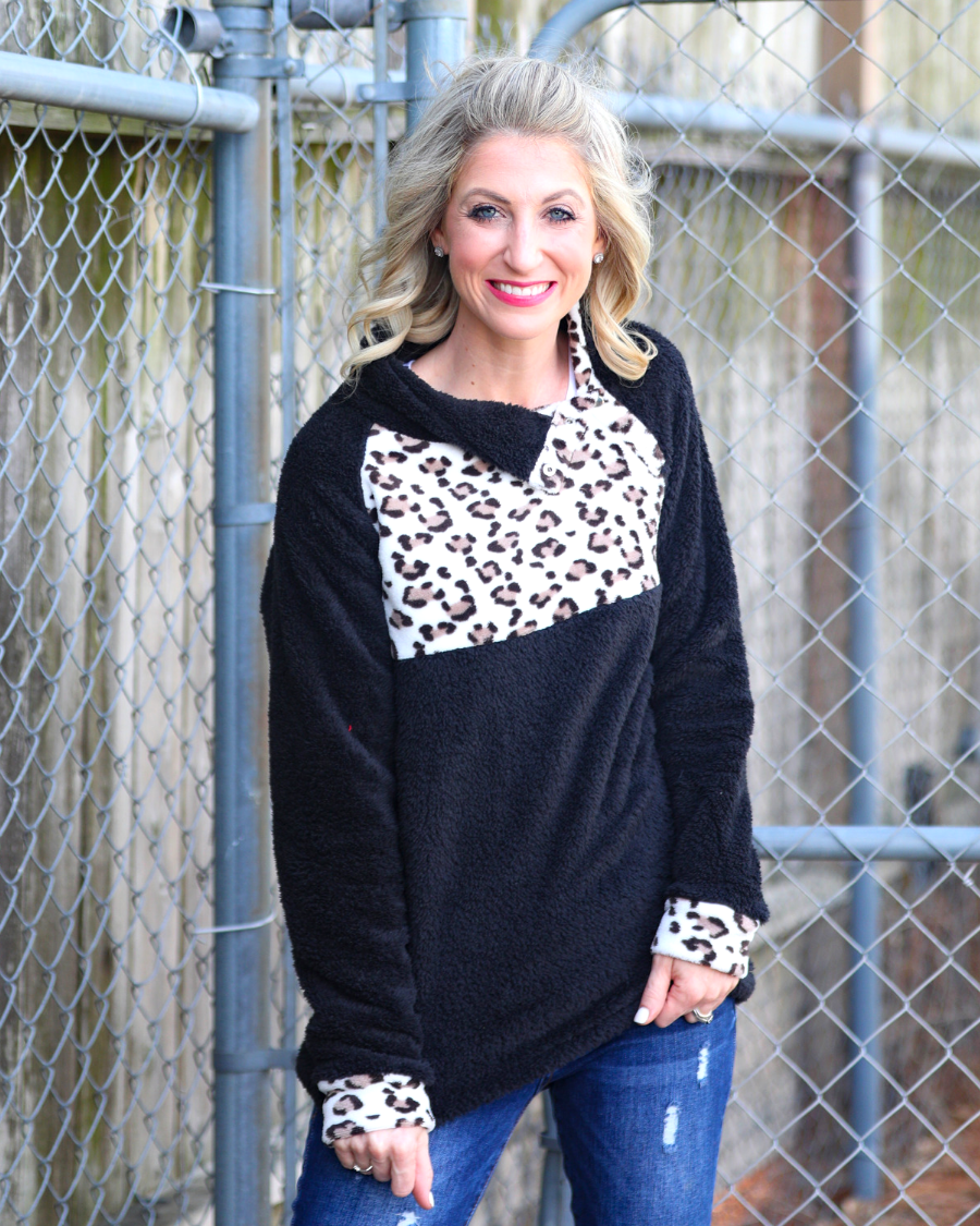 a long-sleeve pullover crafted from plush fleece with a striking ivory leopard accent across the bodice with coordinating leopard cuffs, silver side snap detailing along the shoulder, and a fold over collar