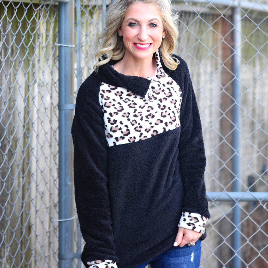 a long-sleeve pullover crafted from plush fleece with a striking ivory leopard accent across the bodice with coordinating leopard cuffs, silver side snap detailing along the shoulder, and a fold over collar