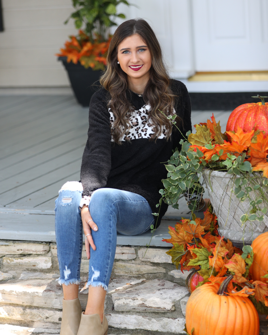 a long-sleeve pullover crafted from plush fleece with a striking ivory leopard accent across the bodice with coordinating leopard cuffs, silver side snap detailing along the shoulder, and a fold over collar