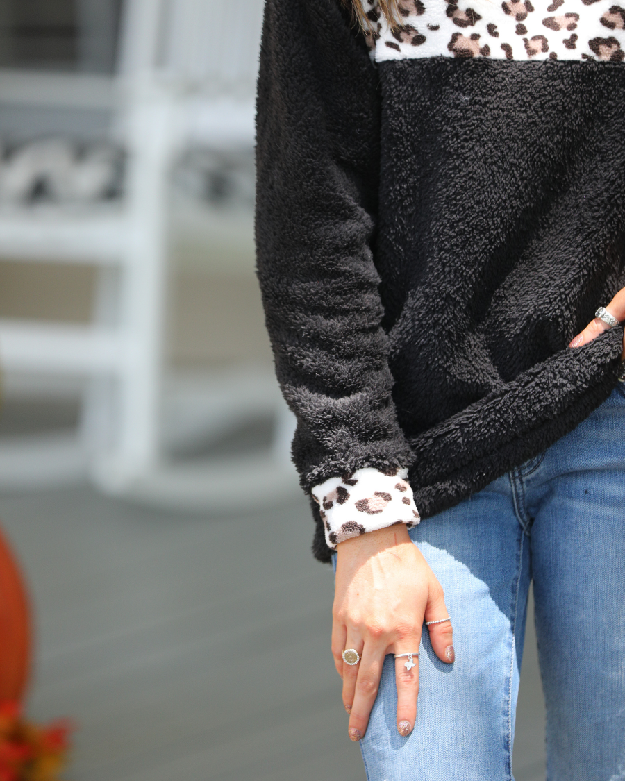 a long-sleeve pullover crafted from plush fleece with a striking ivory leopard accent across the bodice with coordinating leopard cuffs, silver side snap detailing along the shoulder, and a fold over collar