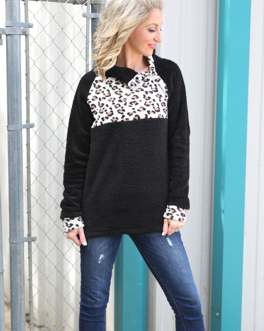 a long-sleeve pullover crafted from plush fleece with a striking ivory leopard accent across the bodice with coordinating leopard cuffs, silver side snap detailing along the shoulder, and a fold over collar