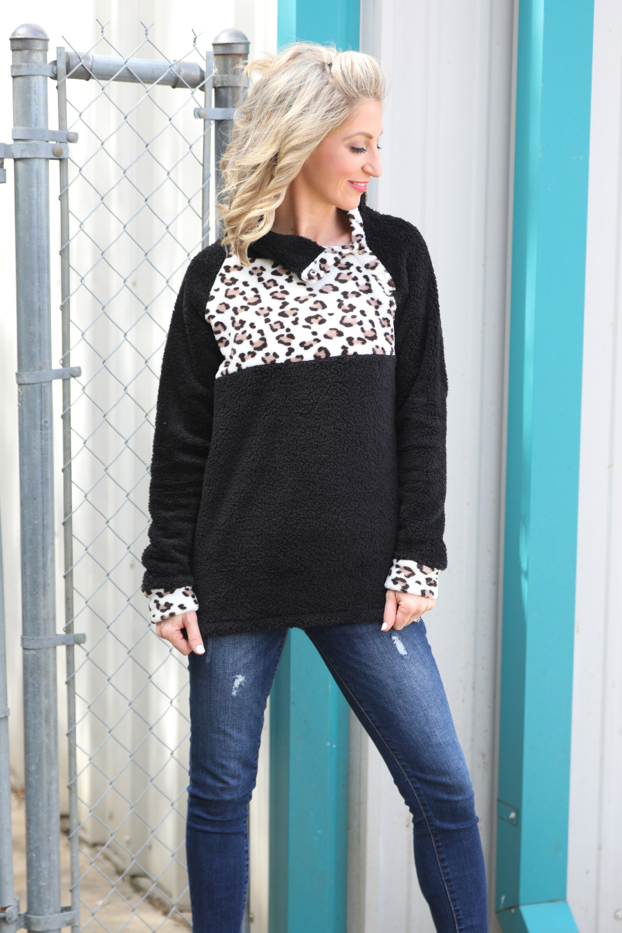 a long-sleeve pullover crafted from plush fleece with a striking ivory leopard accent across the bodice with coordinating leopard cuffs, silver side snap detailing along the shoulder, and a fold over collar