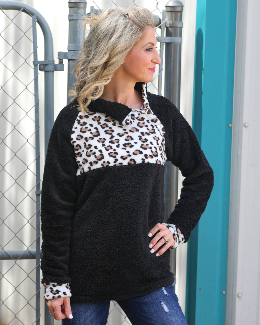a long-sleeve pullover crafted from plush fleece with a striking ivory leopard accent across the bodice with coordinating leopard cuffs, silver side snap detailing along the shoulder, and a fold over collar