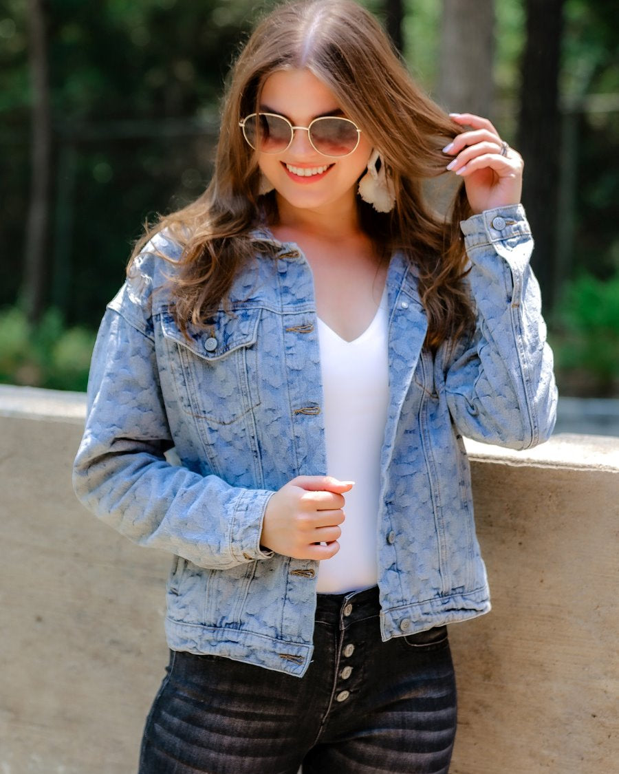 relaxed-fit jacket crafted from light wash denim with subtle distressing and faded leopard print accents, a button-down front, collared neckline, flap chest pockets, rollable long sleeves with buttoned cuffs, and a straight hemline