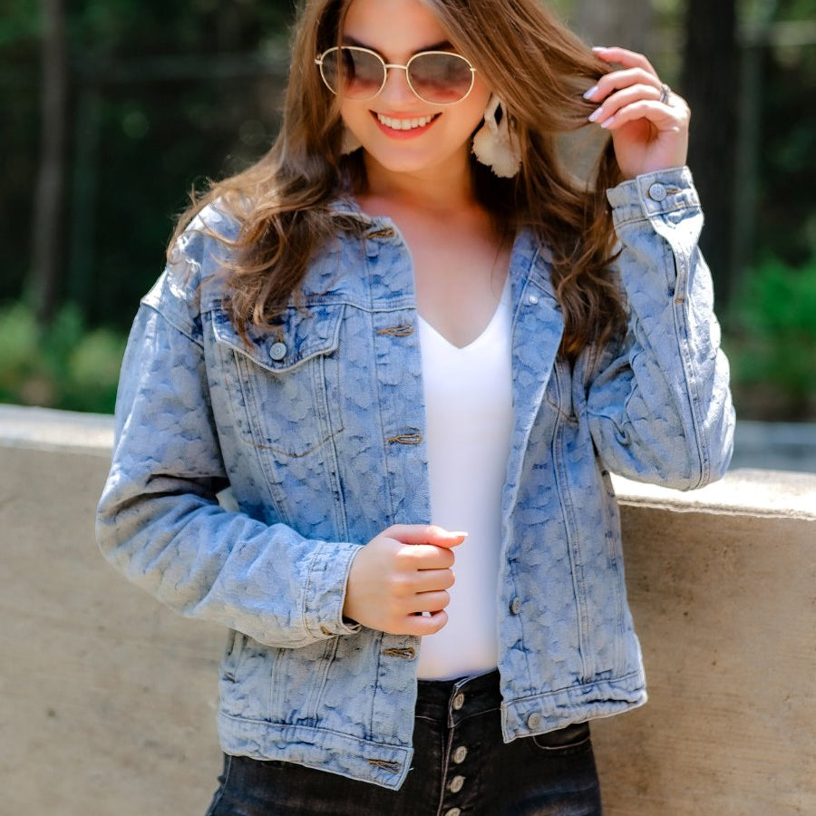 relaxed-fit jacket crafted from light wash denim with subtle distressing and faded leopard print accents, a button-down front, collared neckline, flap chest pockets, rollable long sleeves with buttoned cuffs, and a straight hemline