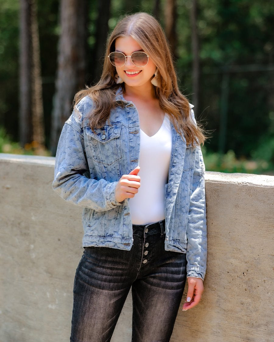 relaxed-fit jacket crafted from light wash denim with subtle distressing and faded leopard print accents, a button-down front, collared neckline, flap chest pockets, rollable long sleeves with buttoned cuffs, and a straight hemline