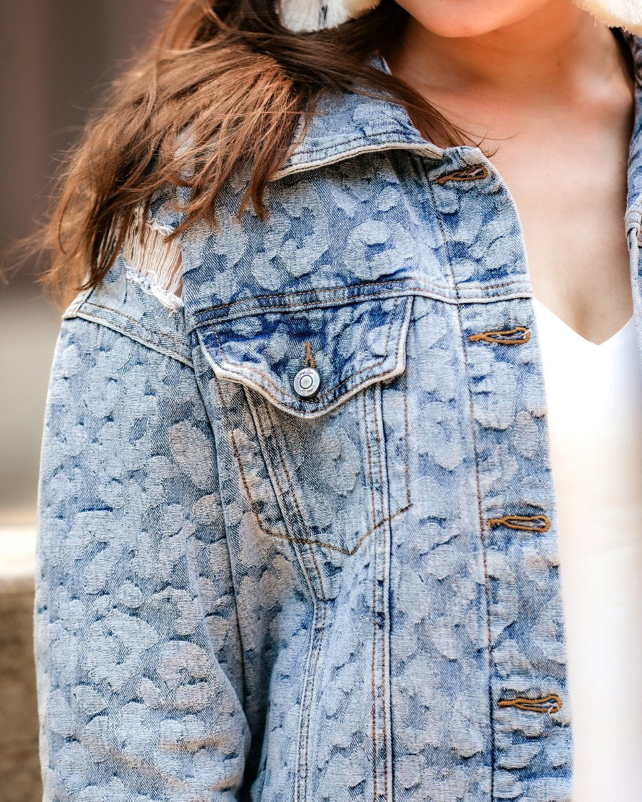 relaxed-fit jacket crafted from light wash denim with subtle distressing and faded leopard print accents, a button-down front, collared neckline, flap chest pockets, rollable long sleeves with buttoned cuffs, and a straight hemline