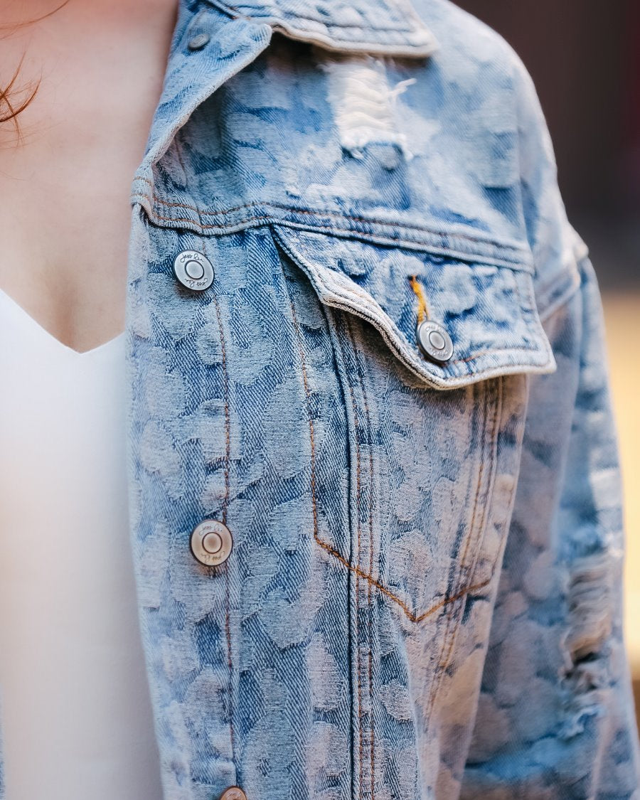 relaxed-fit jacket crafted from light wash denim with subtle distressing and faded leopard print accents, a button-down front, collared neckline, flap chest pockets, rollable long sleeves with buttoned cuffs, and a straight hemline