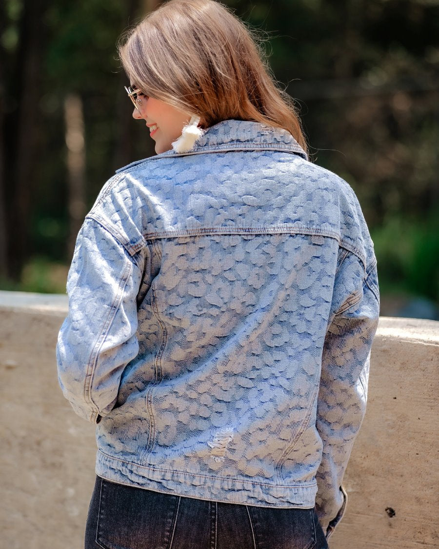 relaxed-fit jacket crafted from light wash denim with subtle distressing and faded leopard print accents, a button-down front, collared neckline, flap chest pockets, rollable long sleeves with buttoned cuffs, and a straight hemline