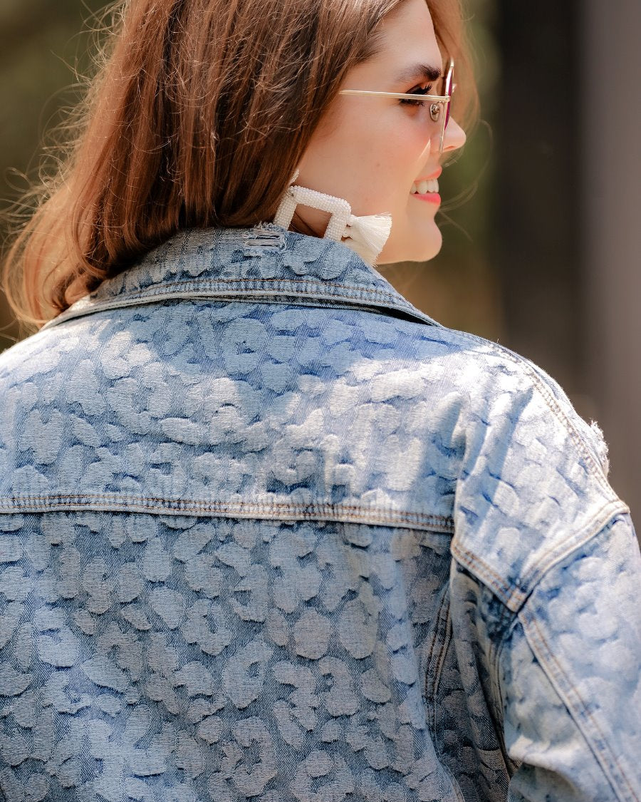 relaxed-fit jacket crafted from light wash denim with subtle distressing and faded leopard print accents, a button-down front, collared neckline, flap chest pockets, rollable long sleeves with buttoned cuffs, and a straight hemline