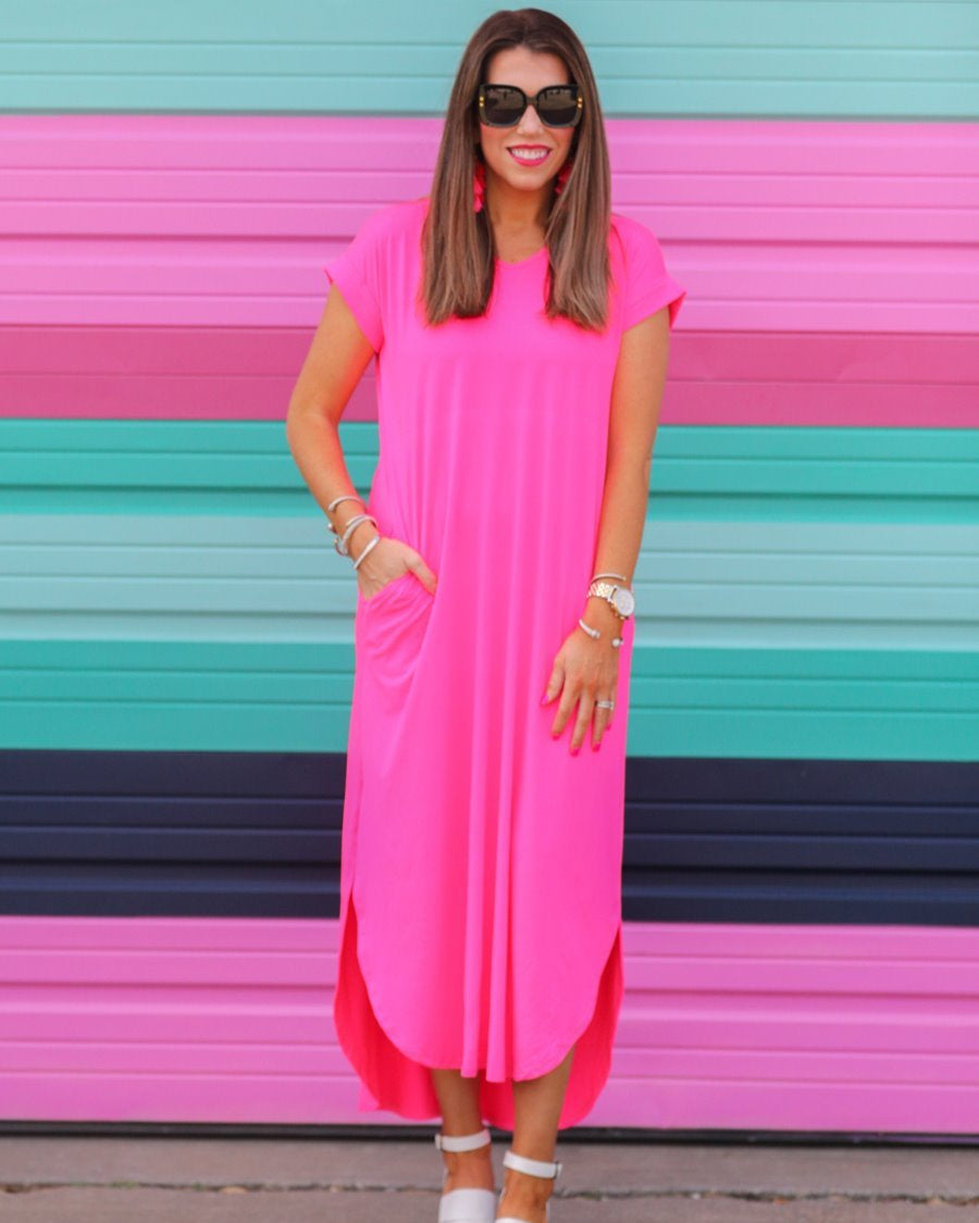 oversized short-sleeve t-shirt dress crafted from soft, stretchy material with a V-neckline, cuffed sleeves, side slits, and pockets on a solid hot pink fabric