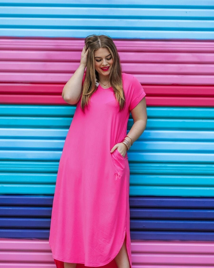 oversized short-sleeve t-shirt dress crafted from soft, stretchy material with a V-neckline, cuffed sleeves, side slits, and pockets on a solid fuchsia fabric