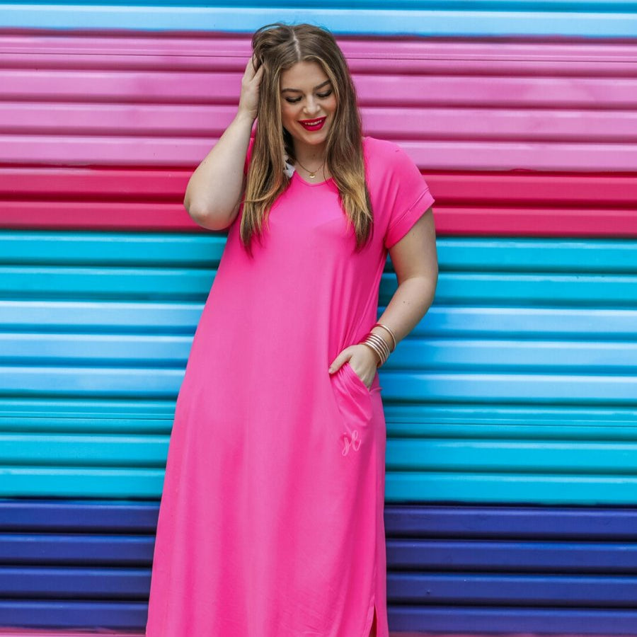 oversized short-sleeve t-shirt dress crafted from soft, stretchy material with a V-neckline, cuffed sleeves, side slits, and pockets on a solid fuchsia fabric