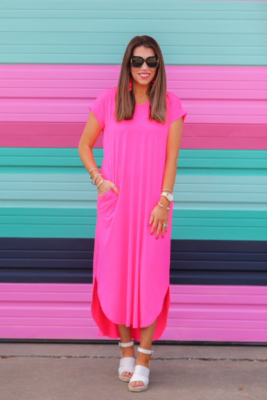 oversized short-sleeve t-shirt dress crafted from soft, stretchy material with a V-neckline, cuffed sleeves, side slits, and pockets on a solid hot pink fabric