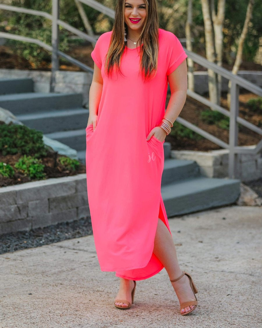 oversized short-sleeve t-shirt dress crafted from soft, stretchy material with a V-neckline, cuffed sleeves, side slits, and pockets on a solid neon coral fabric