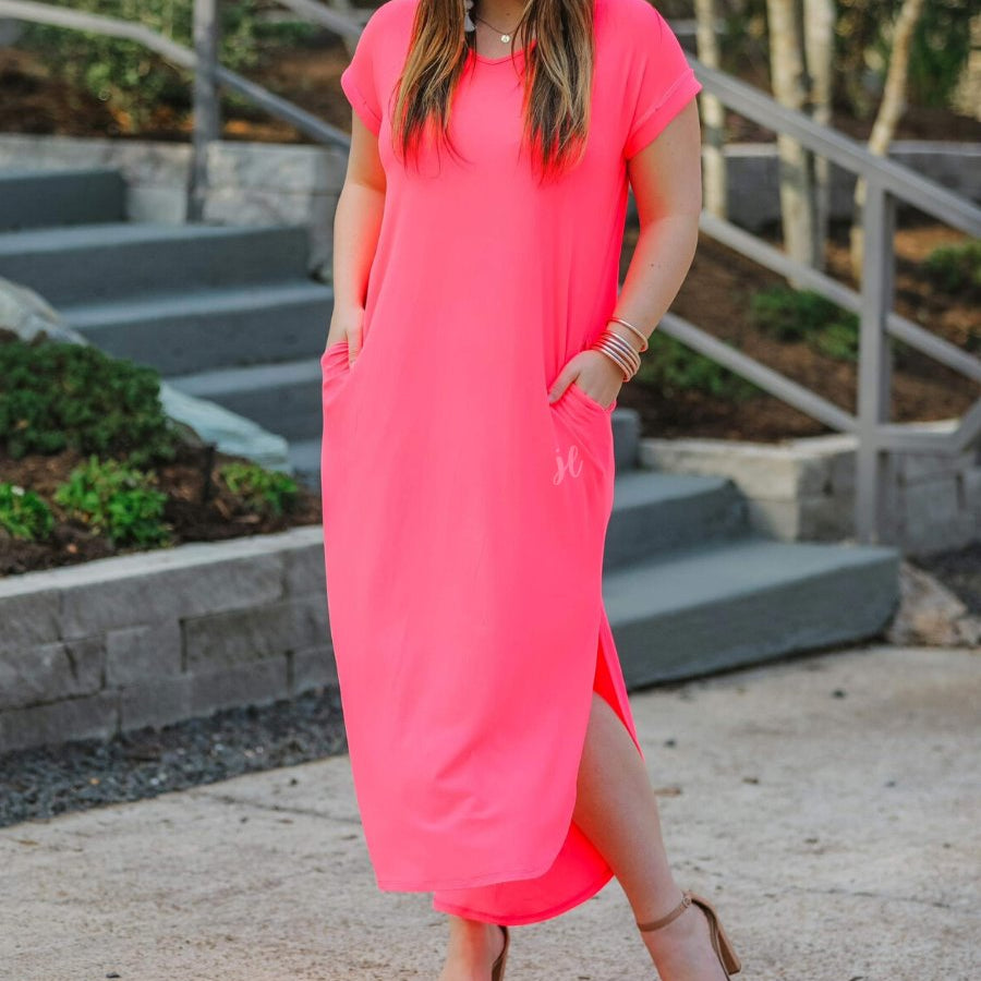 oversized short-sleeve t-shirt dress crafted from soft, stretchy material with a V-neckline, cuffed sleeves, side slits, and pockets on a solid neon coral fabric