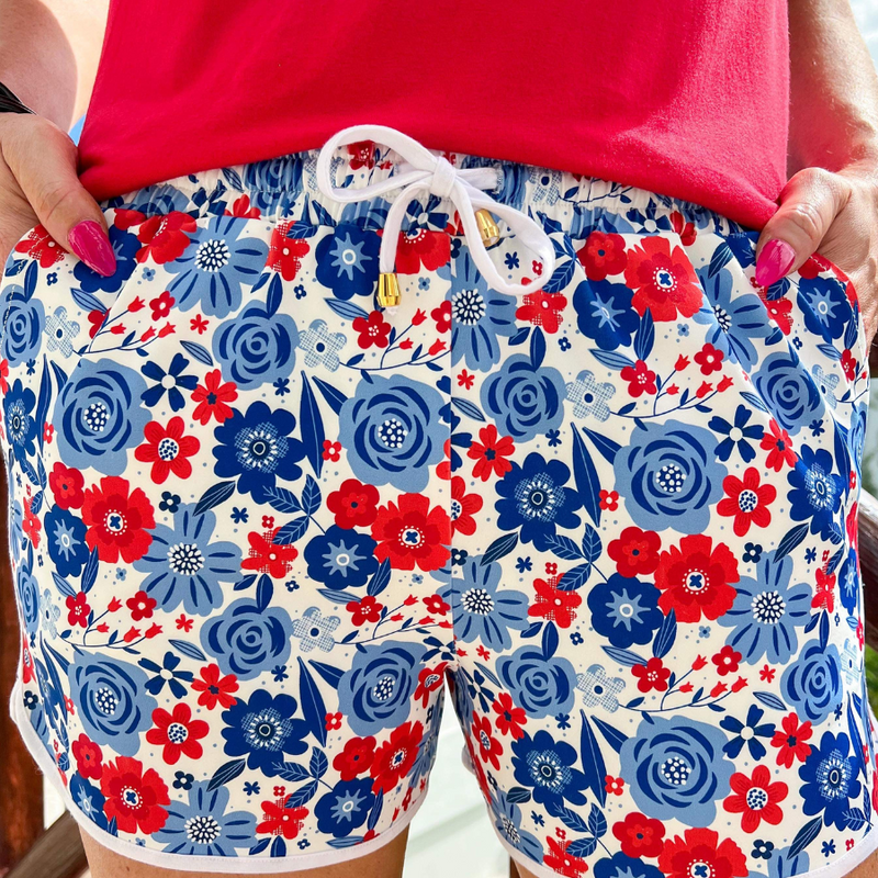 mid-rise relaxed fit activewear shorts with side pockets and a tie waist drawstring with gold bead accents, designed on a patriotic floral pattern print fabric, ivory base, and ivory trim