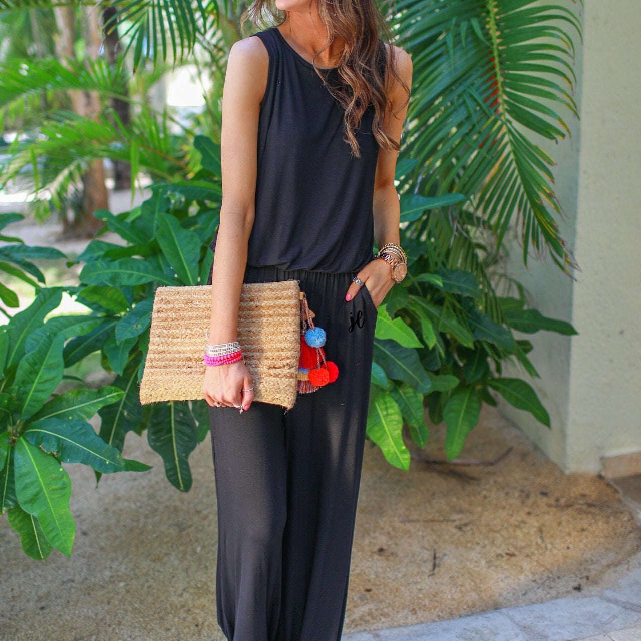 a black sleeveless one-piece jumpsuit with wide 2.5" shoulder straps, a rounded neckline, elastic waist, side pockets, keyhole button back, and a relaxed flare leg silhouette