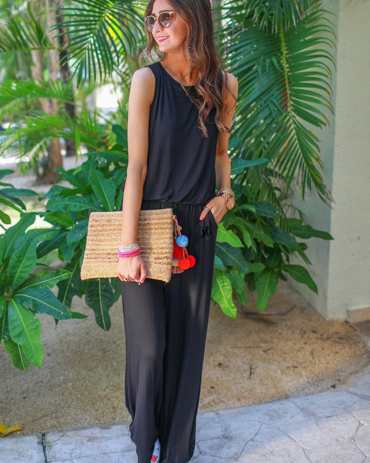 a black sleeveless one-piece jumpsuit with wide 2.5" shoulder straps, a rounded neckline, elastic waist, side pockets, keyhole button back, and a relaxed flare leg silhouette