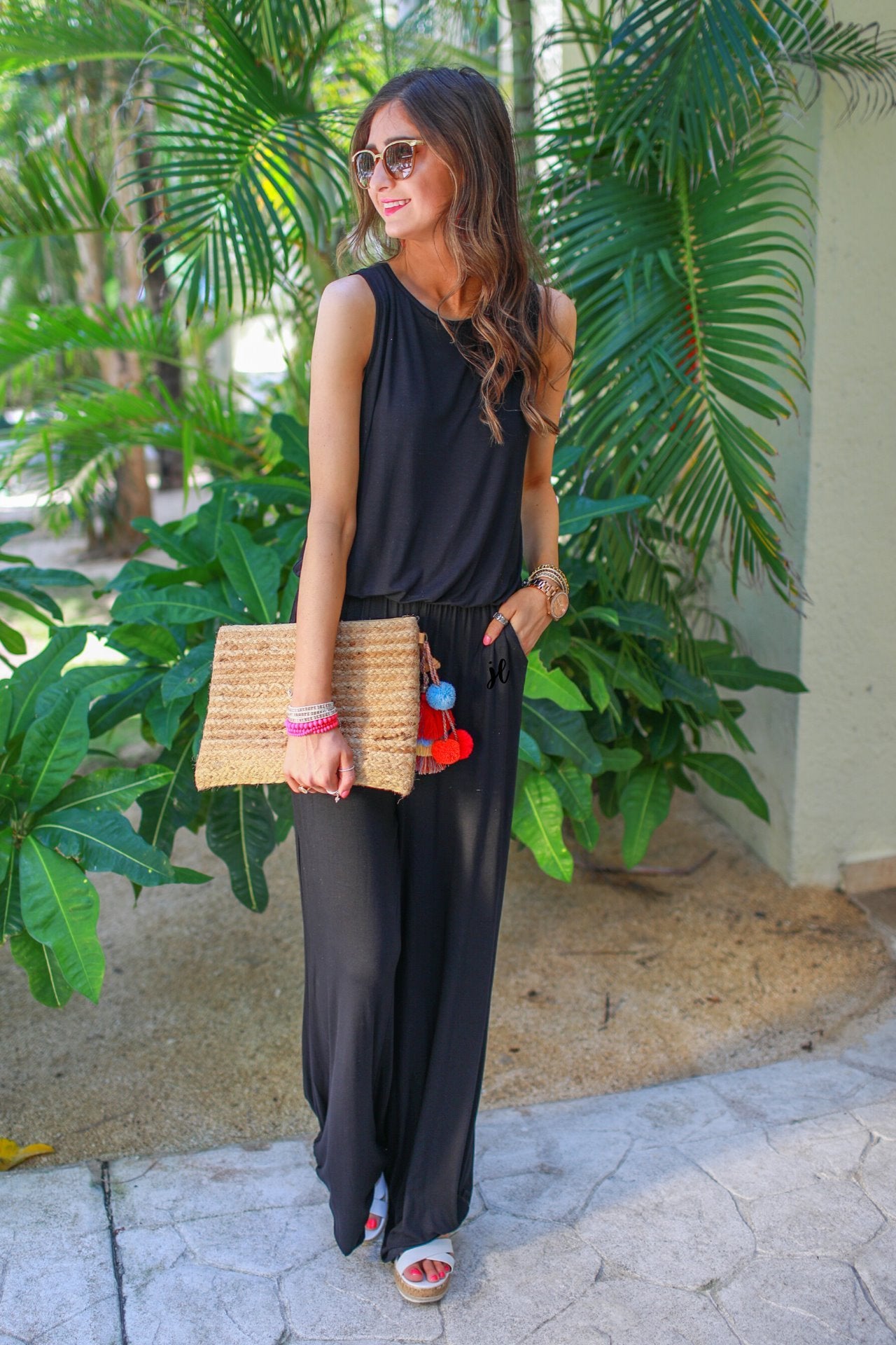 a black sleeveless one-piece jumpsuit with wide 2.5" shoulder straps, a rounded neckline, elastic waist, side pockets, keyhole button back, and a relaxed flare leg silhouette