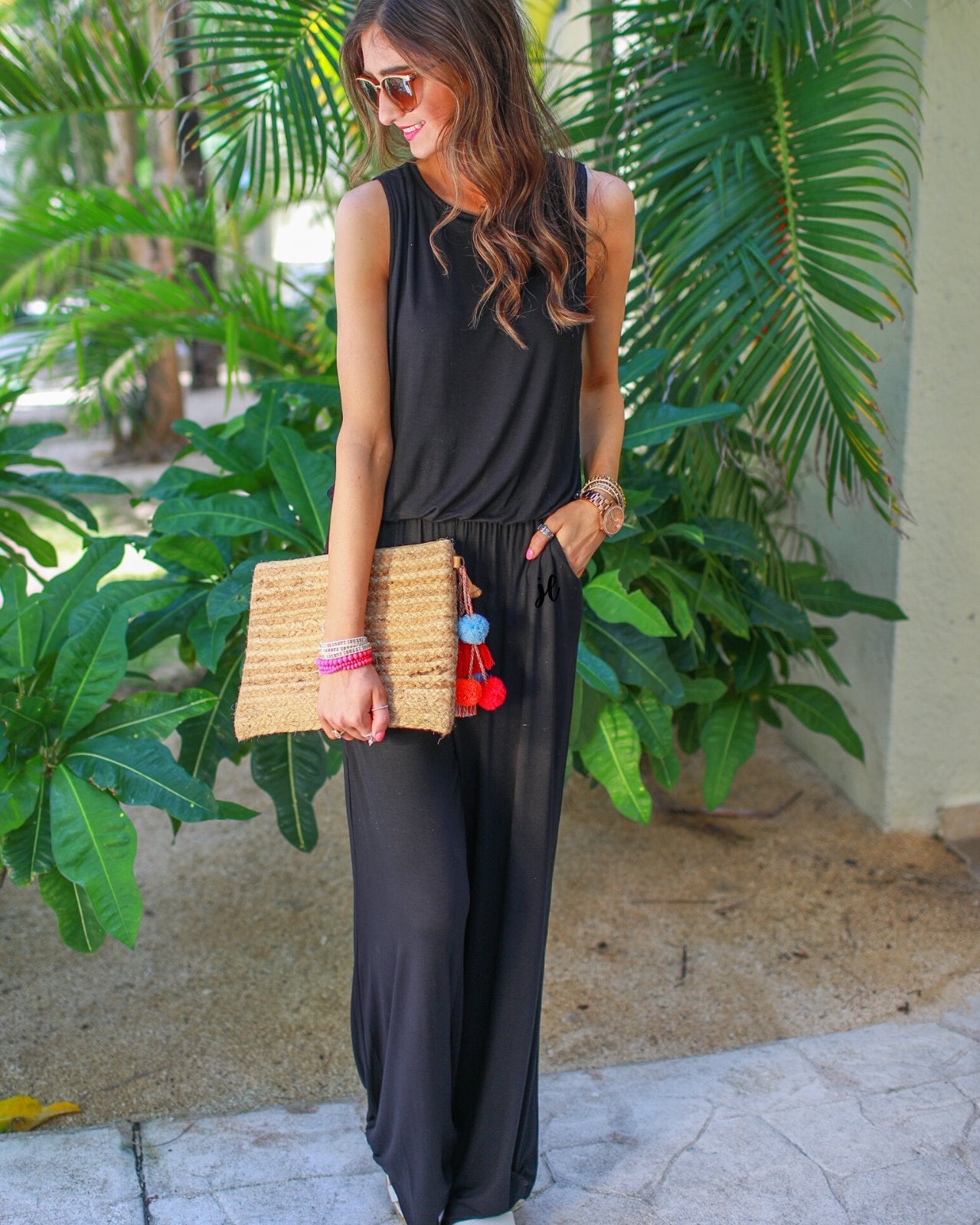 a black sleeveless one-piece jumpsuit with wide 2.5" shoulder straps, a rounded neckline, elastic waist, side pockets, keyhole button back, and a relaxed flare leg silhouette