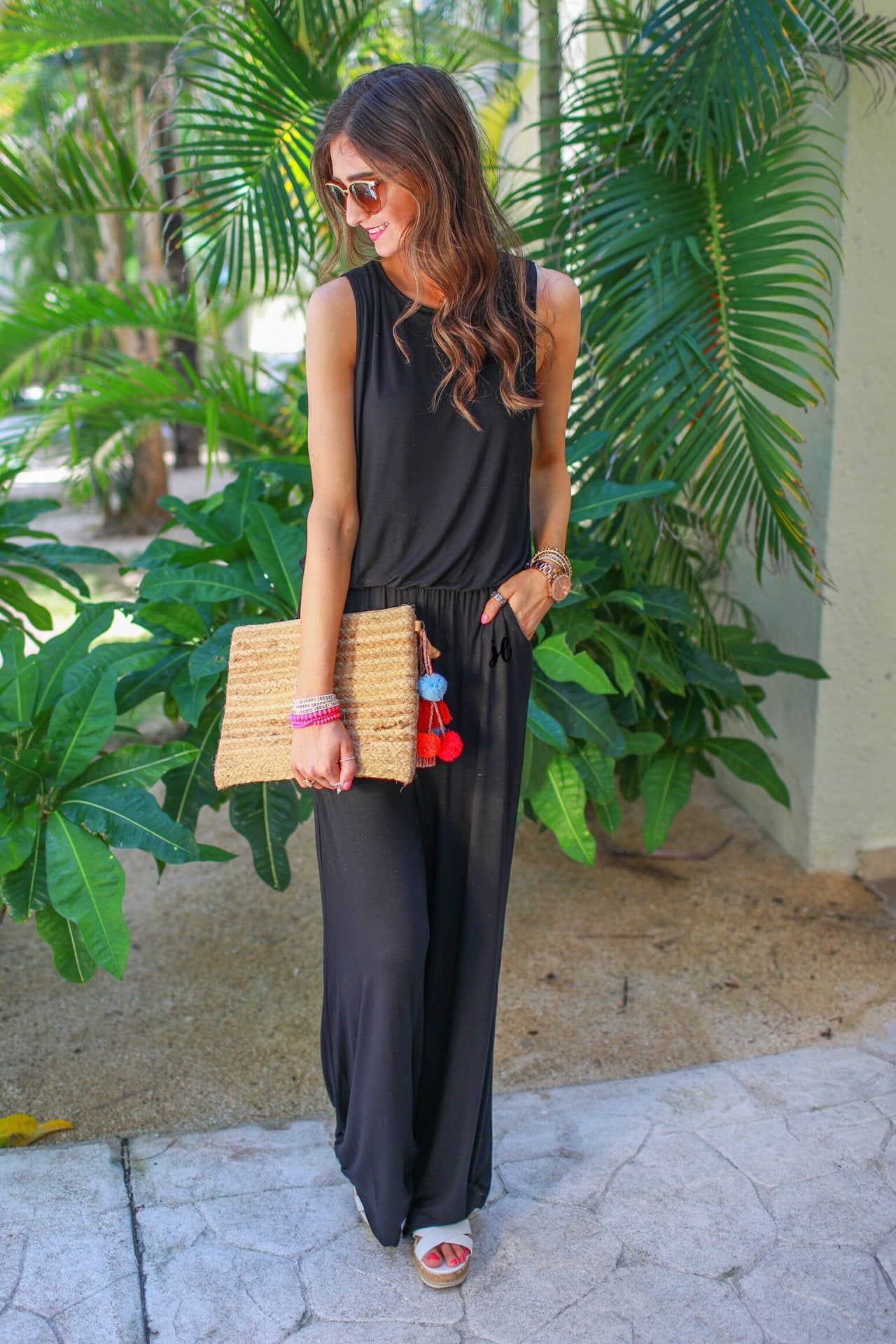 a black sleeveless one-piece jumpsuit with wide 2.5" shoulder straps, a rounded neckline, elastic waist, side pockets, keyhole button back, and a relaxed flare leg silhouette