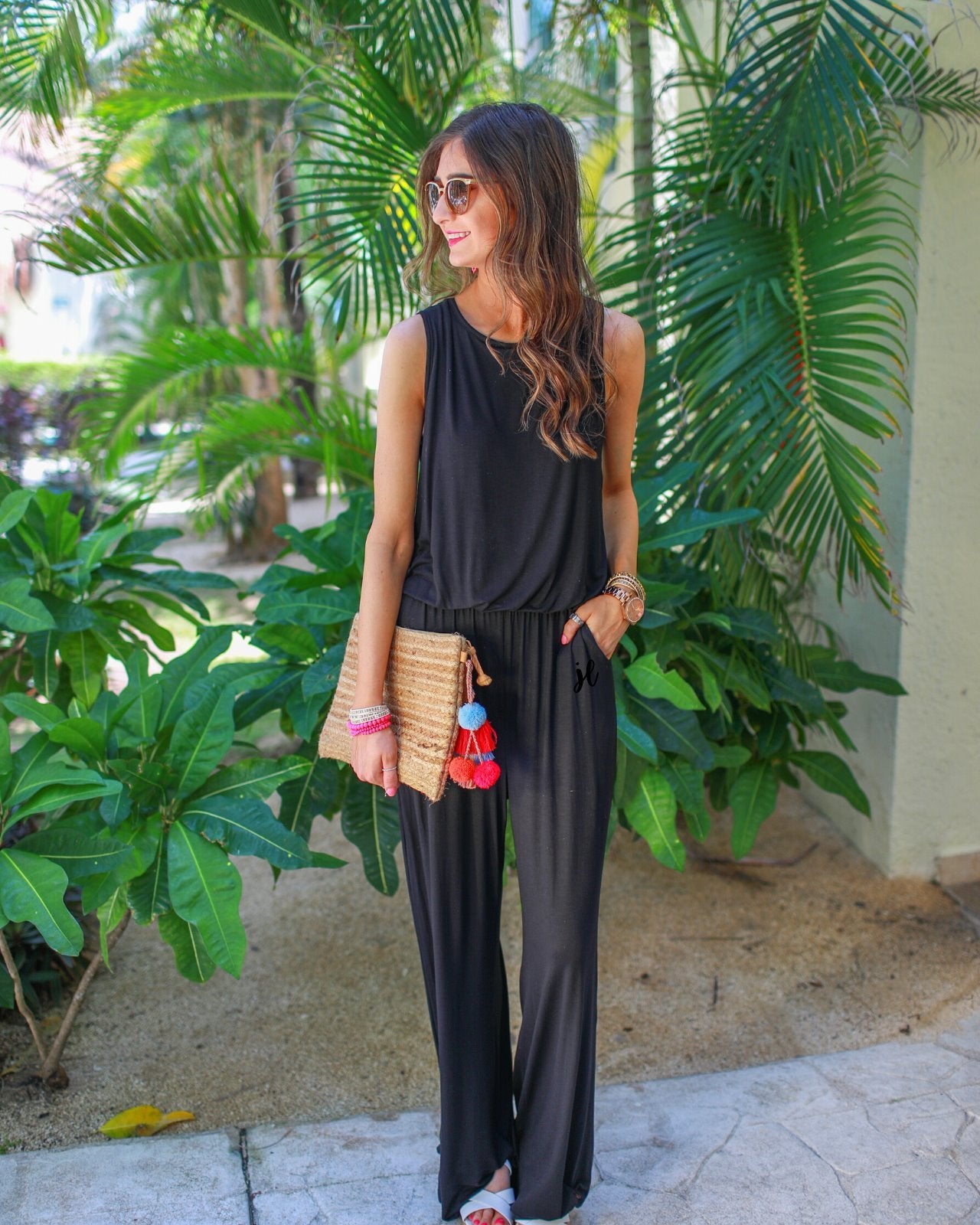 a black sleeveless one-piece jumpsuit with wide 2.5" shoulder straps, a rounded neckline, elastic waist, side pockets, keyhole button back, and a relaxed flare leg silhouette