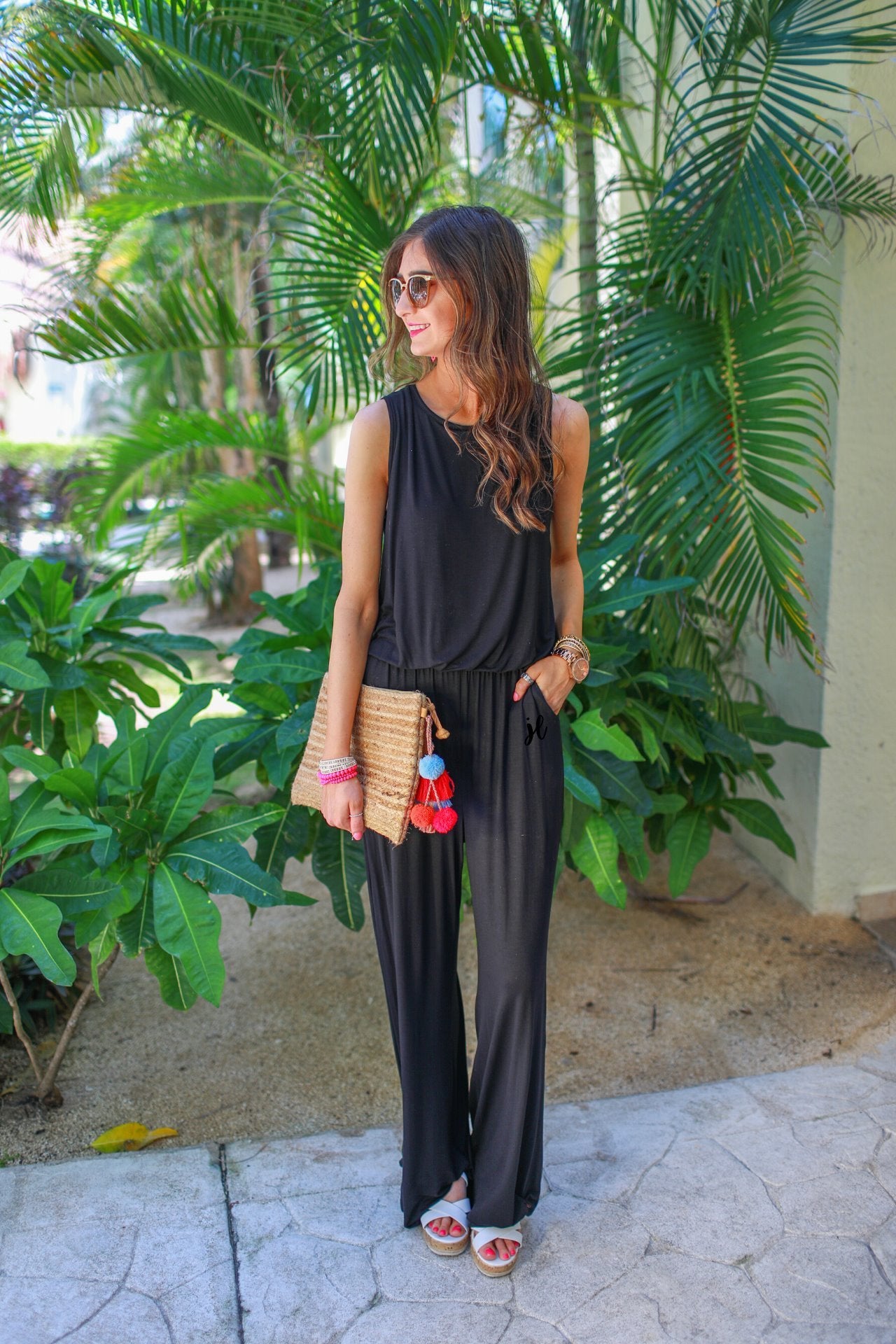 a black sleeveless one-piece jumpsuit with wide 2.5" shoulder straps, a rounded neckline, elastic waist, side pockets, keyhole button back, and a relaxed flare leg silhouette
