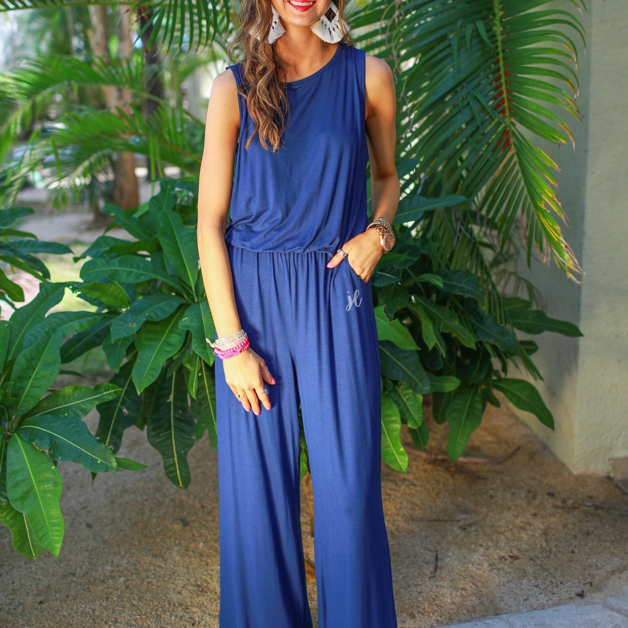 a navy sleeveless one-piece jumpsuit with wide 2.5" shoulder straps, a rounded neckline, elastic waist, side pockets, keyhole button back, and a relaxed flare leg silhouette