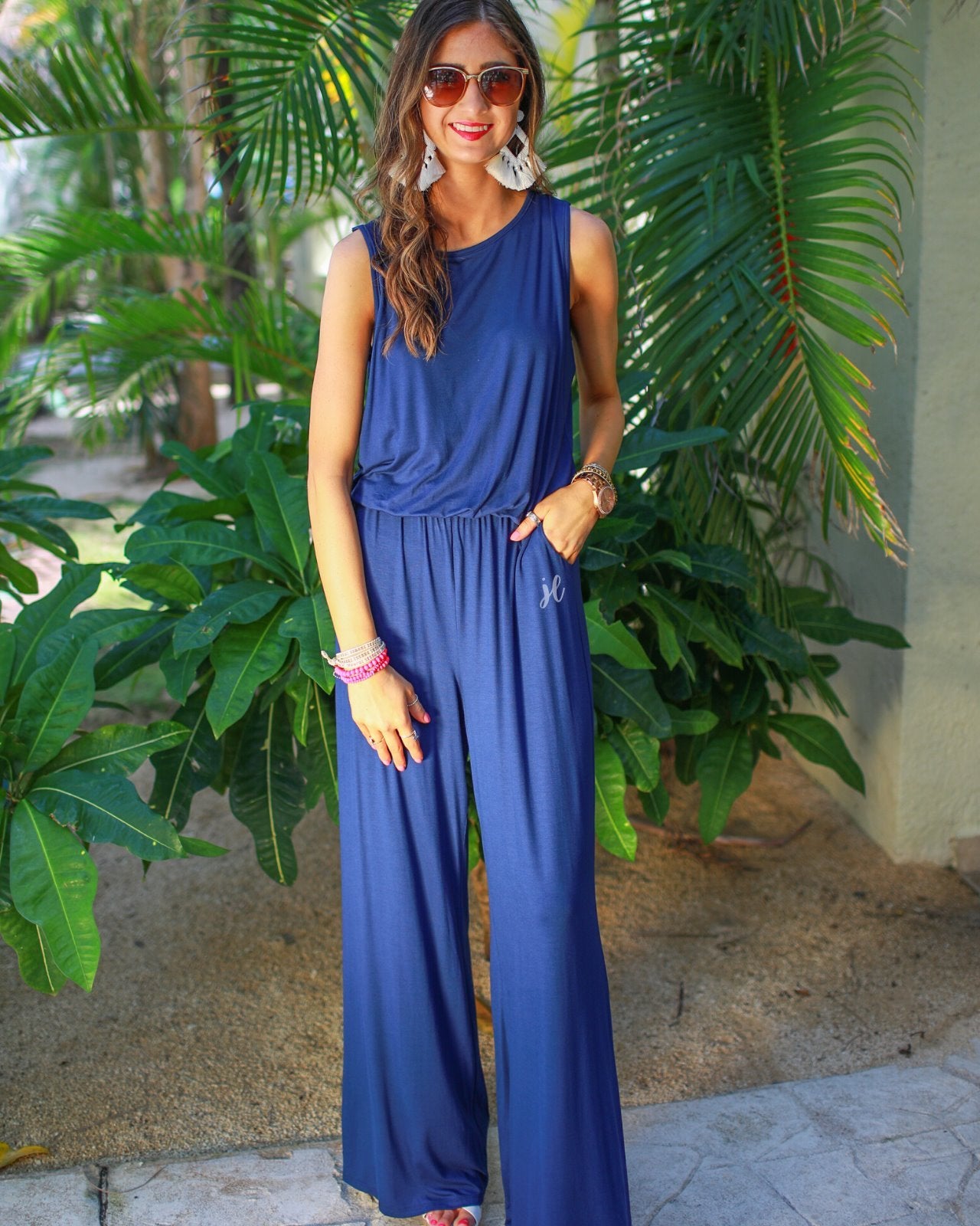 a navy sleeveless one-piece jumpsuit with wide 2.5" shoulder straps, a rounded neckline, elastic waist, side pockets, keyhole button back, and a relaxed flare leg silhouette