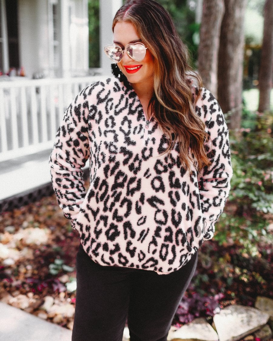 a long-sleeve fluffy pullover with a quarter zip, convenient front pockets, a foldable collar, and an elastic band at the hemline on a pink leopard sherpa fabric